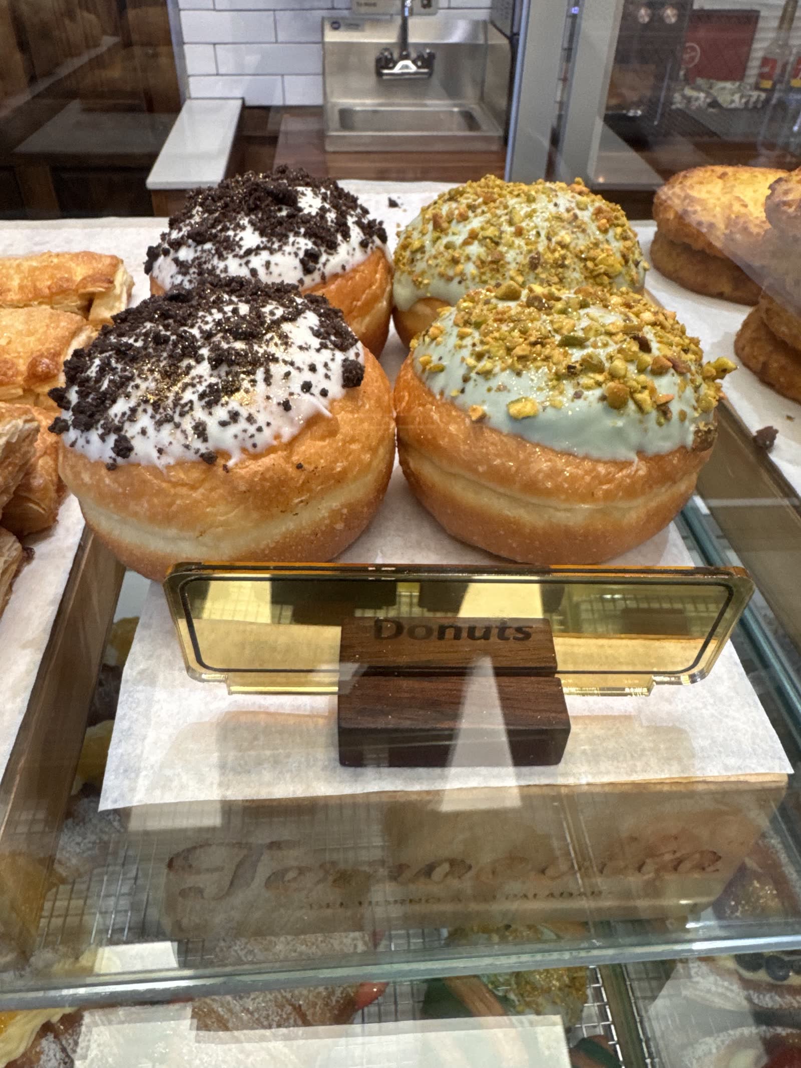 Donuts in the glass case, cookies-and-cream and pistachio, on a Terracotta-branded wood riser