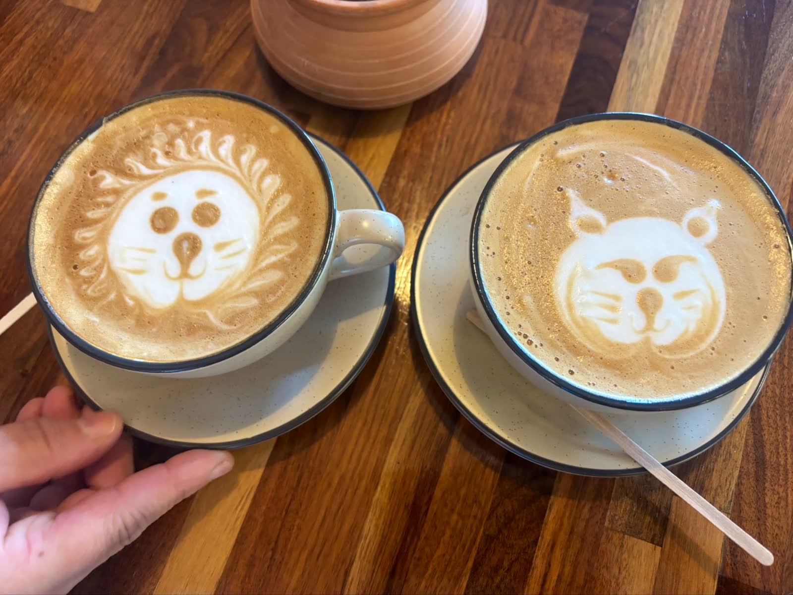 Two lattes with animal-face latte art in cream cups