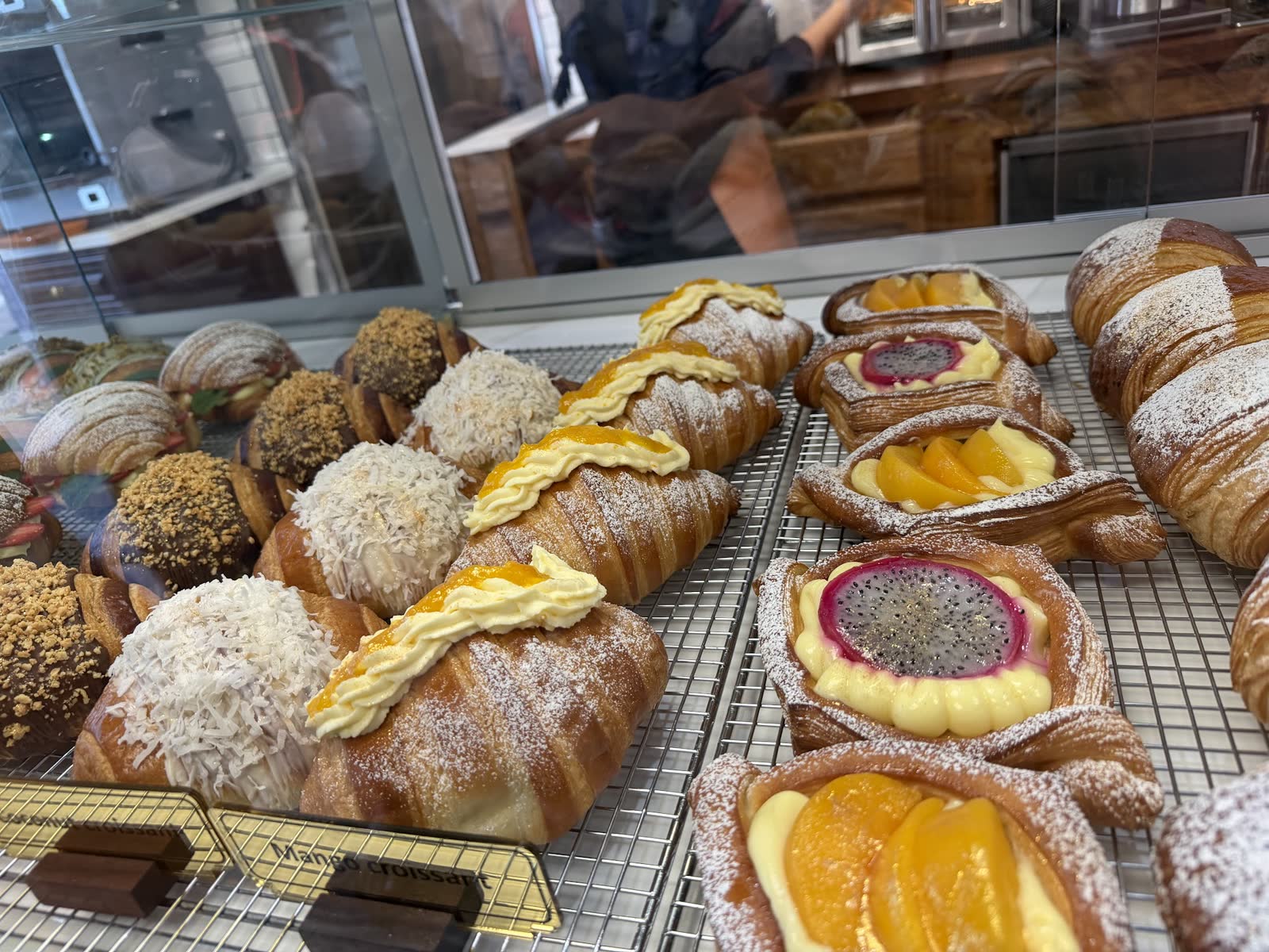 Mango croissants, fruit danishes, and coconut pastries on a rack in the case