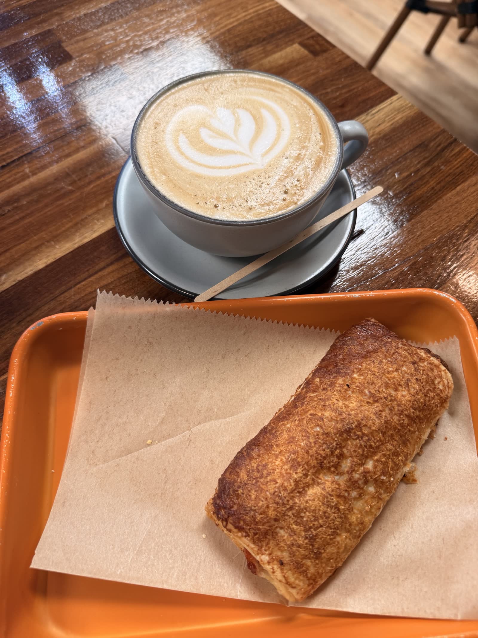 Latte with foam art and a pastry on an orange tray