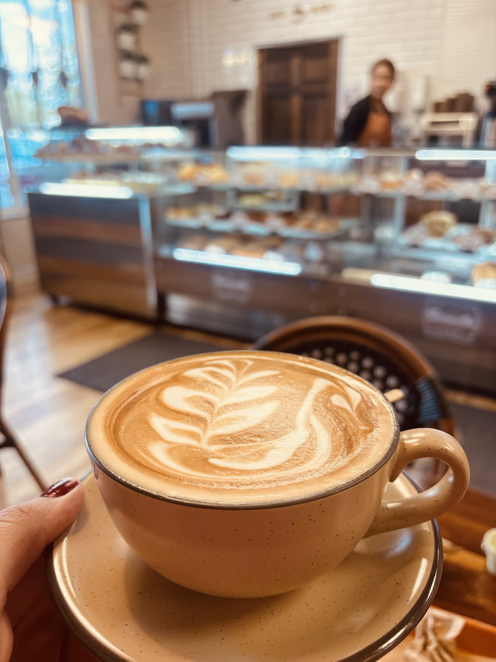 Latte with leaf art held in the dining room, pastry cases in the background