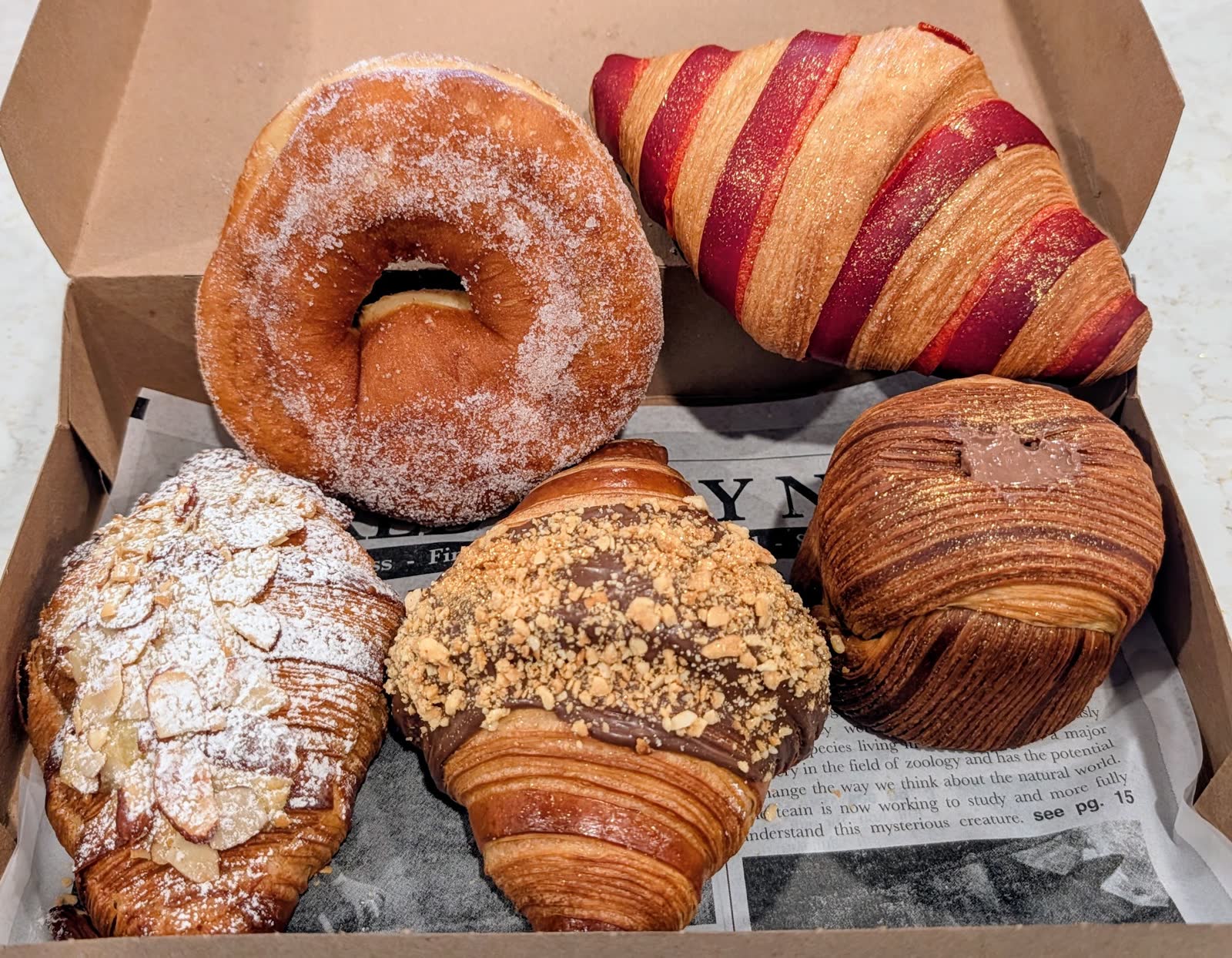 Open bakery box with five pastries including almond and chocolate croissants